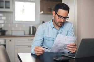 Man with specs reading a bill while holding a credit card